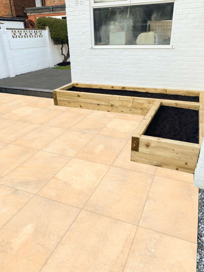 Wooden raised garden beds on a patio with a white wall and window in the background.