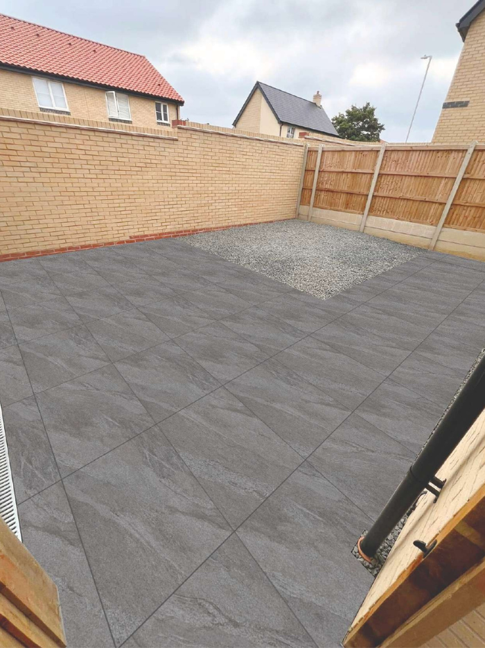 Gray tiled patio area in a backyard with wooden fences and houses in the background.