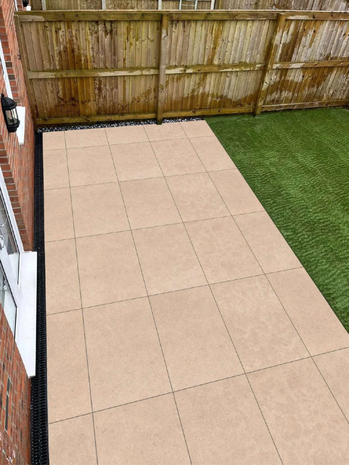 Beige tiles on a patio area with a grassy patch and wooden fence in the background.