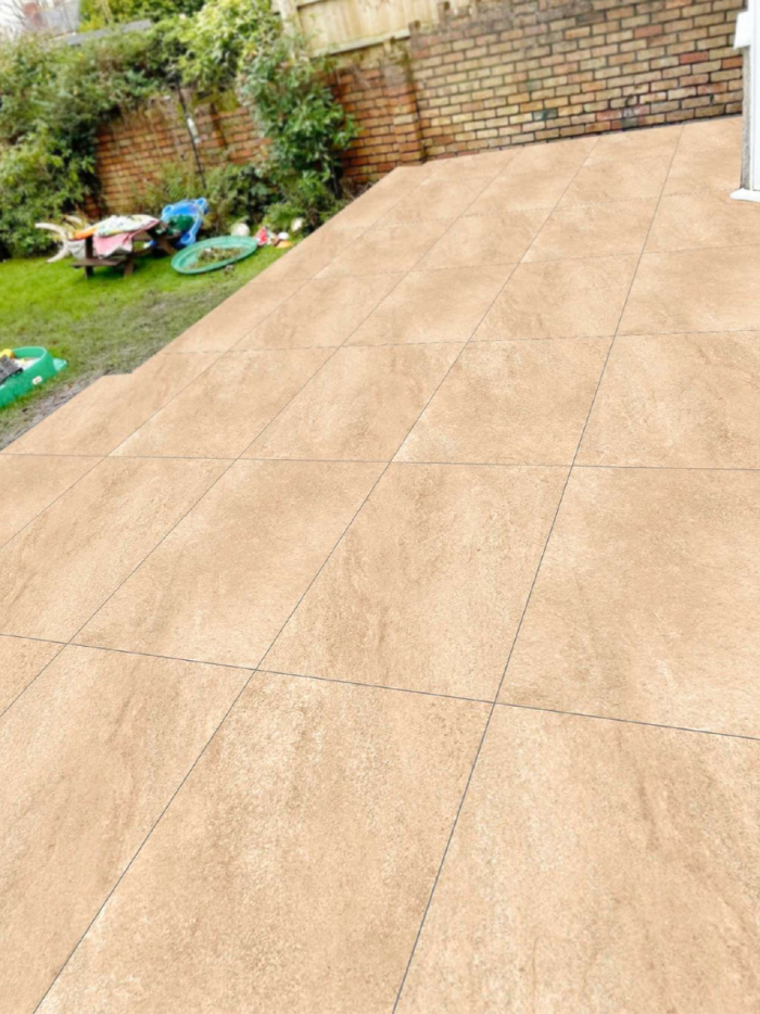 Beige tiles on a patio with a garden and brick wall in the background