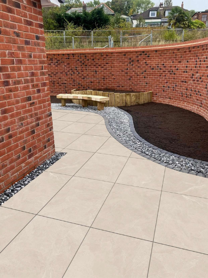 Paved patio area with a brick wall and garden bed in the background